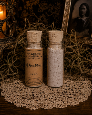 Two vintage-style glass apothecary bottles with cork stoppers sit on a lace doily. One bottle has a tan label reading 'ALVARADO APOTHECARY As You Please' and the other contains a light gray powder.