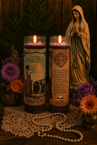 Two lit candles with labels, a statue of a woman, and flowers on a wooden surface.