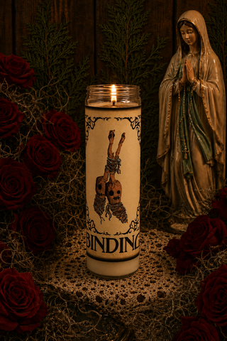Candle with a design and text, surrounded by red roses and a statue of a religious figure.
