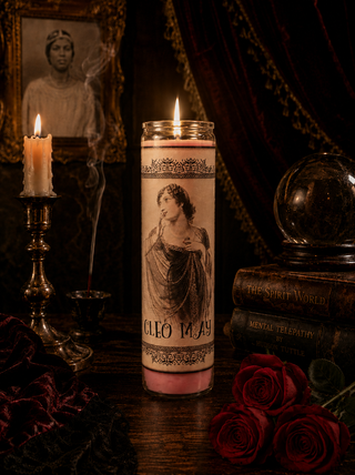 Candle with a printed design of a woman and text, surrounded by red roses and a mirror.
