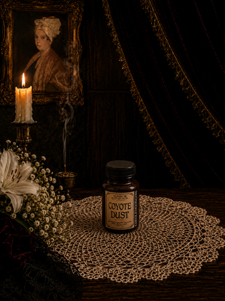 Jar of 'Coyote Dust' on a doily with a candle and portrait in the background