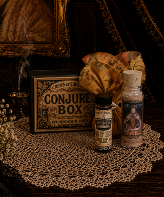 Two bottles with labels and a decorative Crown of Success conjure box on a doily with a dark background