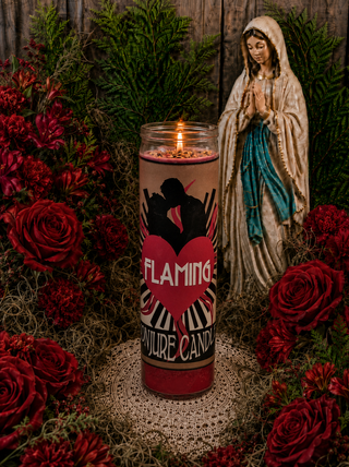 Candle with 'Flaming' branding in front of a statue and flowers