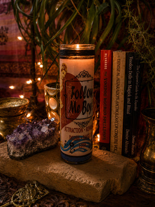 Candle labeled 'Follow Me Boy' on a stone surface with books and crystals in a mystical setting.