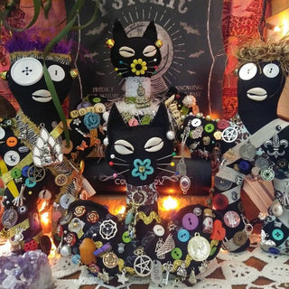 A highly detailed, gothic-themed altar display featuring three black cat figurines adorned with colorful flowers, silver charms, pentagrams, and buttons, alongside other mystical and occult decorations including crystals, candles, and a tapestry.