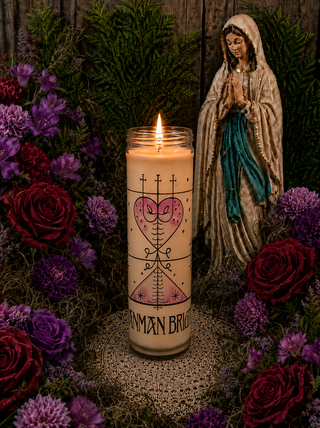 Candle with a design and text, surrounded by flowers and a statue of a religious figure.