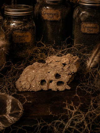 Three jars labeled 'Cemetery Dirt', 'Graveyard Dirt', and 'Crossroads Dirt' with a mud dauber nest in front on a dark background.