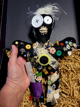 Handmade decorative ju ju doll with buttons and beads held by a hand on a textured surface.