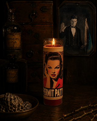 Candle with a graphic design of a woman's face and text, surrounded by a bottle and decorative items.