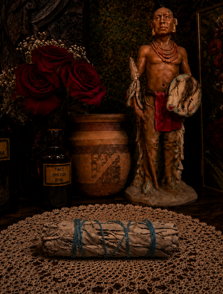 Statue of a Native American figure with a bundle of sage and a jar in a dark setting
