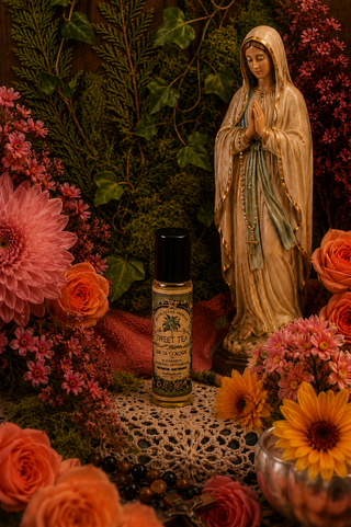 Statue of a religious figure surrounded by flowers and a bottle of Sweet Tea perfume oil by Alvarado Apothecary.