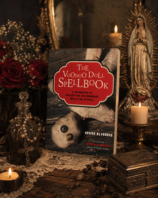 Book titled 'The Voodoo Doll Spellbook' on a dark, mystical background with candles and flowers.