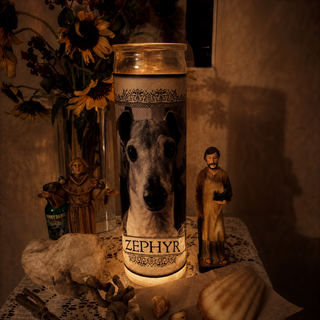 Candle with a dog's face and name 'Zephyr' on a table altar with decorative items.