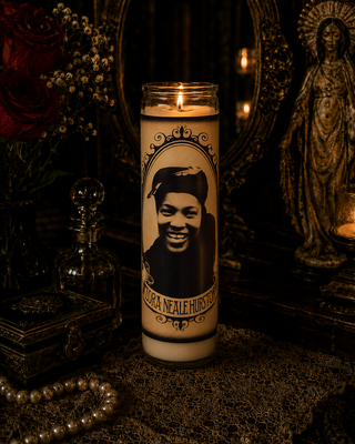 Candle with a portrait on it in a dark setting with flowers and a mirror.