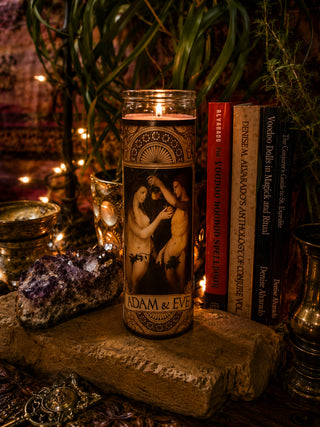 Candle with 'Adam & Eve' design on a stone surface with books and crystals in the background