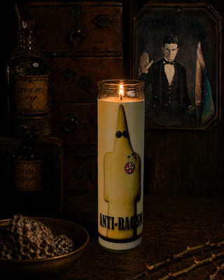 Candle with a banana design and 'Anti-Racism' text on a dark background with bottles and a portrait.
