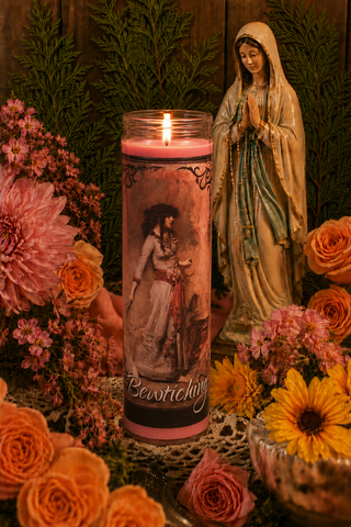 Candle with a printed design of a woman, surrounded by flowers and a statue, on a wooden surface.