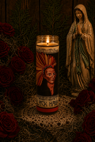 Candle with a portrait and text in front of a statue and red roses