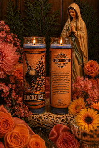 Two Blockbuster candles with a statue of a religious figure and flowers in the background