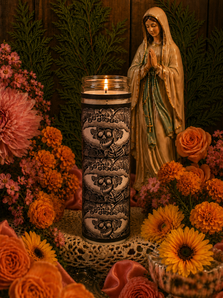 Decorative Calavera candle with intricate designs, surrounded by flowers and a statue of a religious figure.
