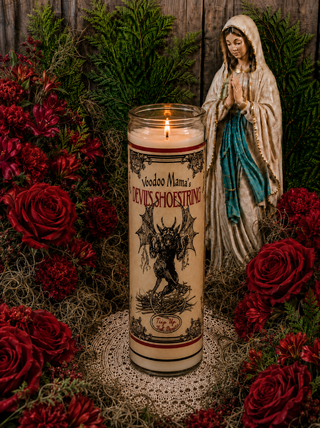 Candle with 'Voodoo Mama's Devils Shoestring' design, surrounded by red roses and a figurine of a woman in a white dress.