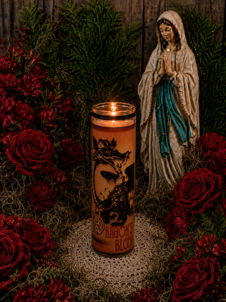 Candle with a dragon design in front of a statue of a woman surrounded by red flowers.